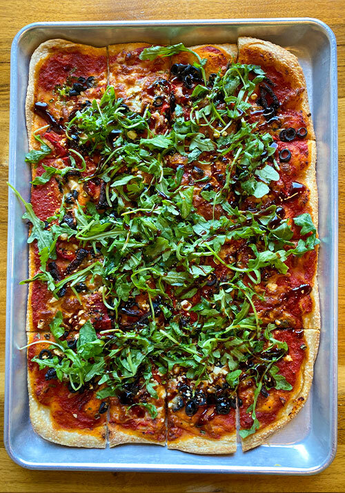 A rectangle tray of vegetable pizza topped with bright green arugula